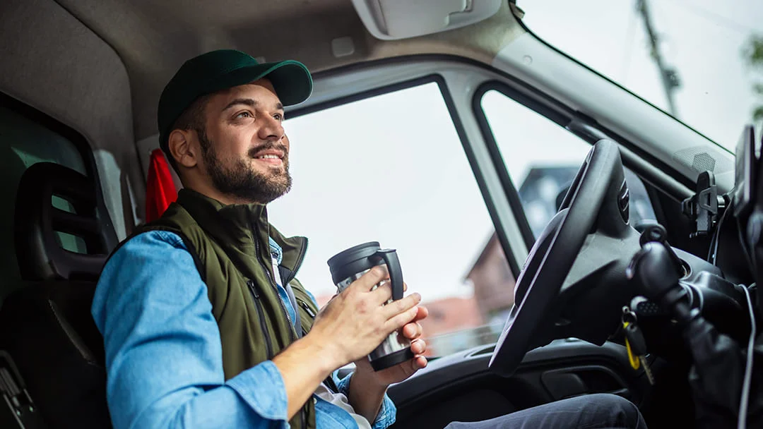 Un homme dans un camion tient une tasse de café, prêt à commencer sa journée de travail.