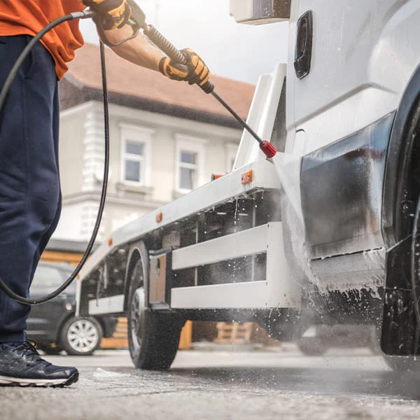 Un homme lave un camion à l'aide d'un nettoyeur haute pression, projetant de l'eau sur la carrosserie brillante.