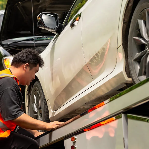 Un homme travaille sur une voiture, utilisant des outils pour effectuer des réparations nécessaires.