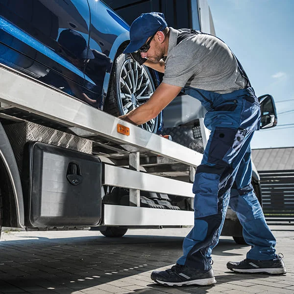 Un homme charge une voiture bleue sur un camion plateau, prêt à être transportée vers sa destination.