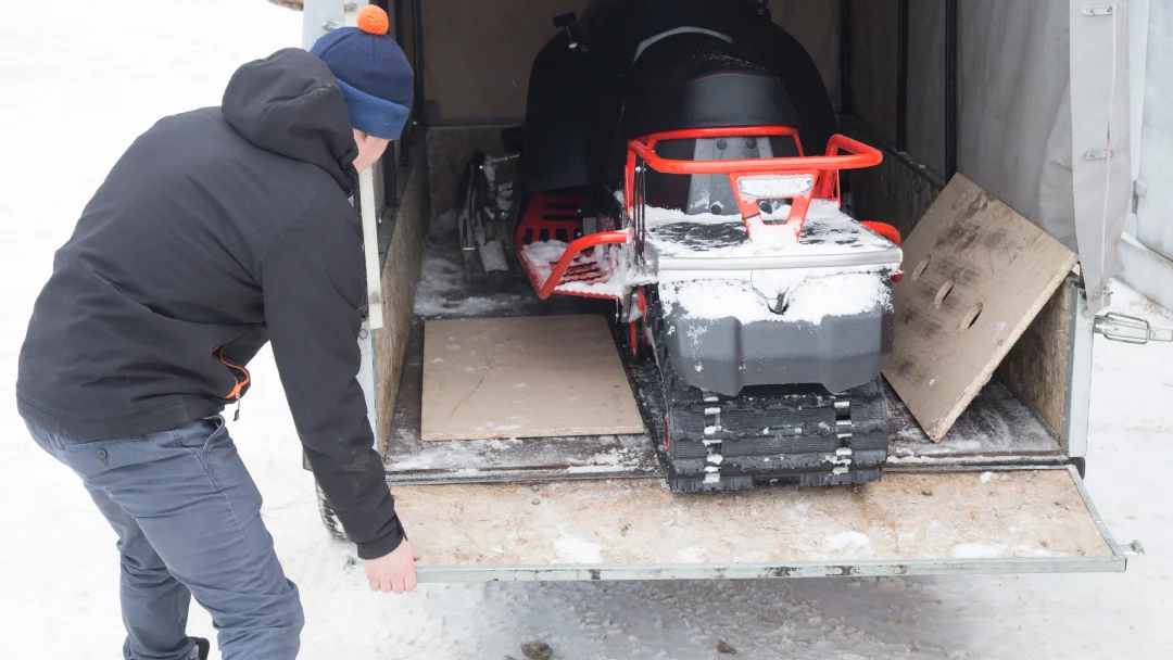 Un homme charge une motoneige dans une remorque, préparant son transport pour une aventure hivernale.