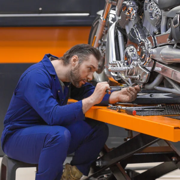 Un homme effectue des réparations sur une moto à l'aide d'un élévateur moto dans un atelier.