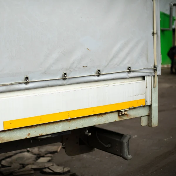 Camion blanc avec une bande jaune sur le côté, utilisé pour le transport de toiles de remplacement.