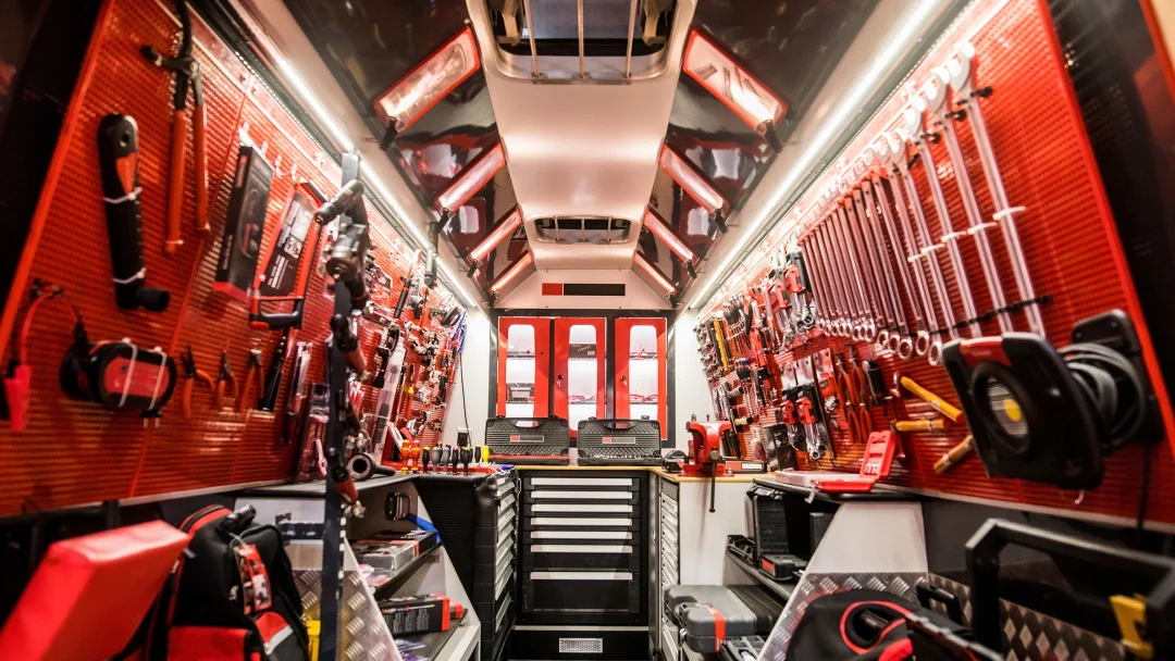 Camion rouge et noir avec des outils accrochés aux murs, équipé d'un accessoire de remorque.