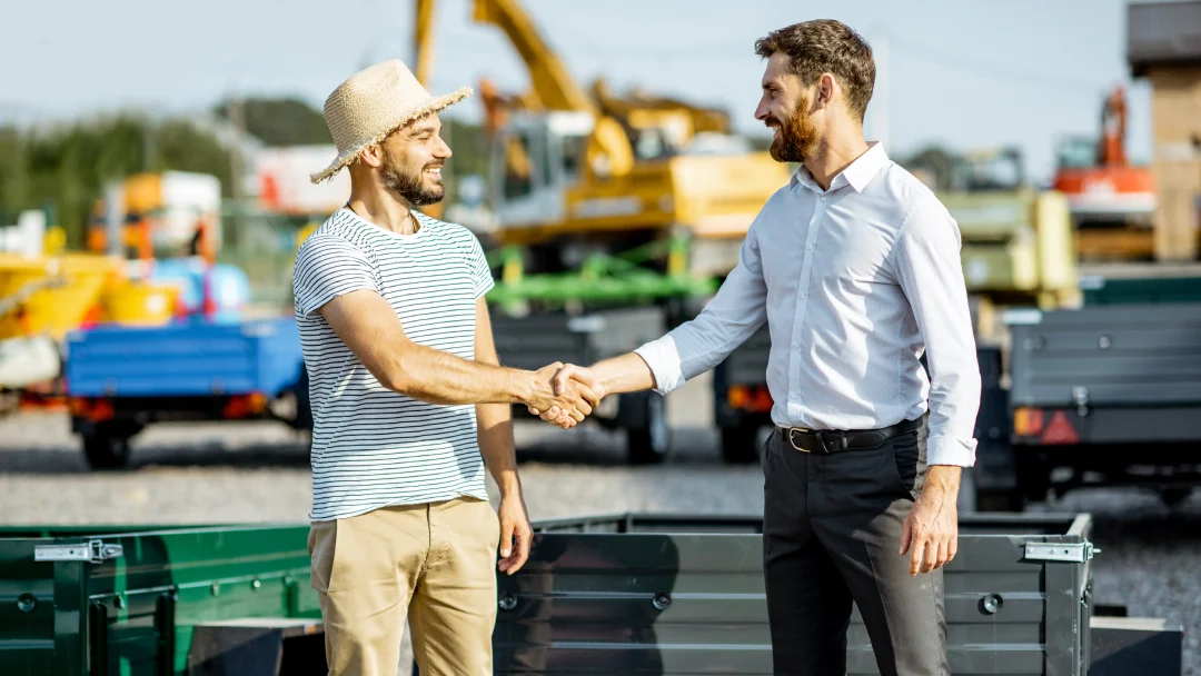 Deux hommes se serrent la main devant un camion, symbolisant un accord sur des remorques d'occasion.