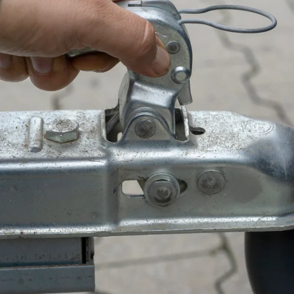 Une personne tient un attache remorque en métal, illustrant un accessoire essentiel pour le transport de charges.
