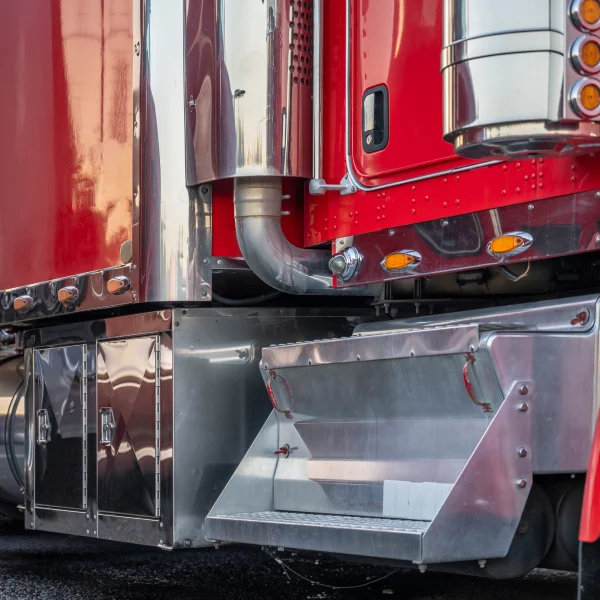 Gros plan sur un camion semi-remorque rouge, mettant en évidence les marchepieds et les détails de la carrosserie.