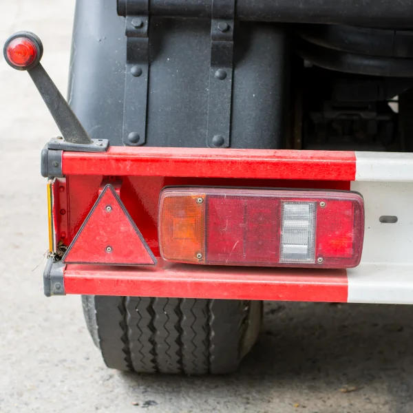 Camion rouge et blanc avec un triangle sur le pare-choc arrière, stationné sur une route.